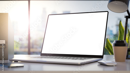 Leinwand Poster A laptop with a blank frameless screen mockup template is positioned in angled position on a table in an office interior, offering a front view, with office buildings in the background