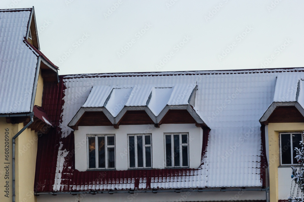 Snow on the roof of a red, brown metal roof of a European house with a window