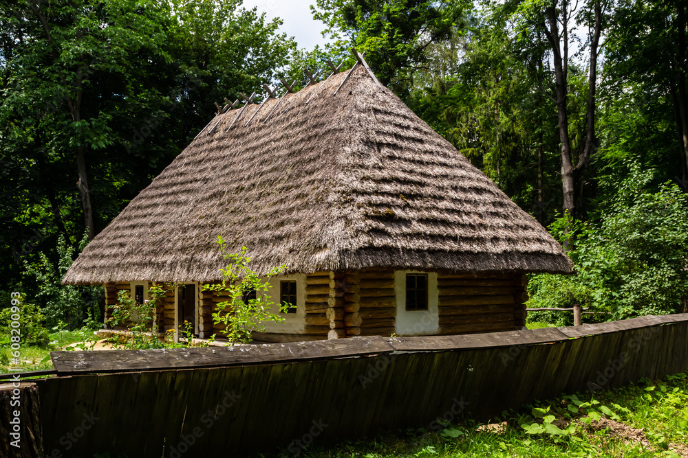 Traditional Ukrainian old house under a thatched roof on the background of the forest on a summer sunny day Traditional Ukrainian old house under a thatched roof on the background of the forest on a summer sunny day