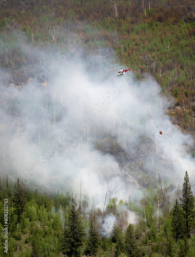 A helicopter carries a bucket of water over forest fire smoke in Kootenay National Park, British Columbia, Canada