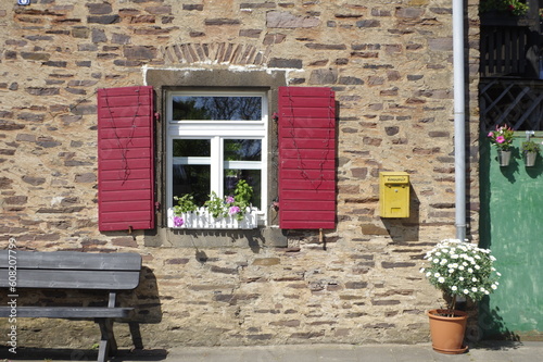 Ein Fenster in einer Natursteinwand mit roten Fensterläden in Mörz in der Eifel