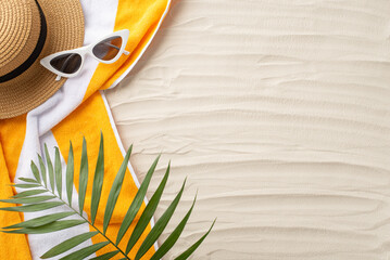 Beach paradise awaits. Top view of summer accessories: sunglasses, headwear, yellow towel, and palm leaves. Sandy shore backdrop with an empty space for text or ads