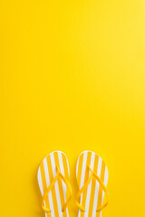 Delight in the beauty of summer with this eye-catching top vertical view flat lay. Discover a pair of flip-flop shoes on a bright yellow background, with a blank space for your text or advertisement