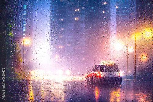 View through glass window with rain drops on blurred city street after rain and colorful neon bokeh city lights, night street scene. Focus on raindrops on glass