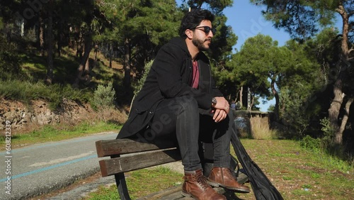 Guy sits  on the back of a bench by the road and take in the sights and sounds of this tranquil environment