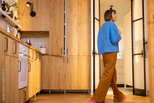 Kitchen interior with female person walking. Stylish interior of studio apartment made wooden materials. Domestic lifestyle