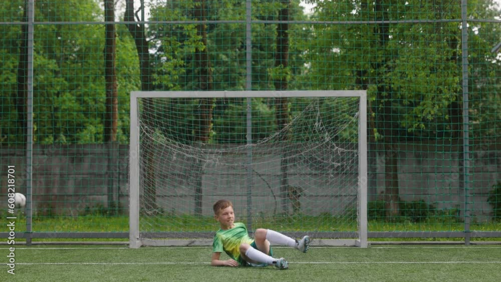 The boy dressed in football uniform is practicing on a mini football stadium. The young footballer tries to do bicycle scissor kick but misses the goal. Front shot The boy dressed in football uniform is practicing on a mini football stadium. The young footballer tries to do bicycle scissor kick but misses the goal. Front shot