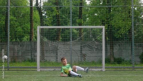 The boy dressed in football uniform is practicing on a mini football stadium. The young footballer tries to do bicycle scissor kick but misses the goal. Front shot photo