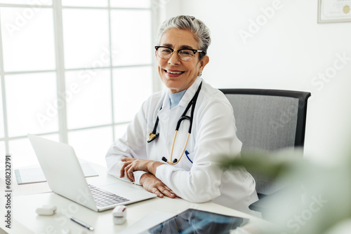 Friendly female physician smiling at the camera in her office, wearing a lab coat and a stethoscope