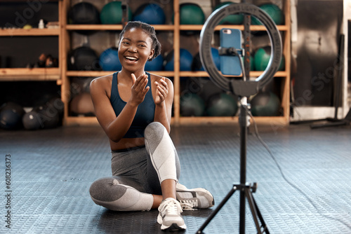 Fitness, woman and phone blog for live stream exercise at gym on platform or app. Influencer, training or health vlog with black person or coach talking to social media or virtual audience with light photo