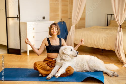 Young woman meditates while doing yoga, spending leisure time with her cute dog at home. Concept of mental health and balance, friendship with pets