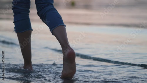 Evening promenade by the sea. Serenity of a girl walking barefoot by the shoreline at dusk. Sunset