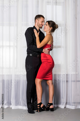 Handsome well dressed young man in black and beautiful woman in red dress are closely looking at each other. The romantic couple exchange loving gazes at each other. © Georgi