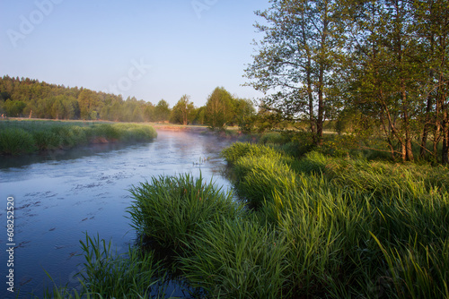 Beatiful scenery of river and green meadow on sunrise. Fresh morning in summer on the river. The river winding with green coasts. Light mist risesover river and meadow after sunrise. 