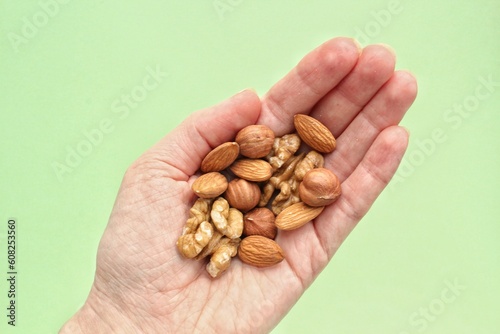 Almond, hazelnut, walnut  in the palm of outstretched hand on green background. Healthy eating diet, nutrition, vegan concept. Protein organic food. Dry snack. National nut day. Copy space for text