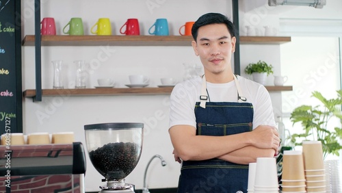 Portrait of attractive young asian men barista in apron standing with arms croessed smiling while looking at camera in coffee shop counter. Coffee business owner concept photo