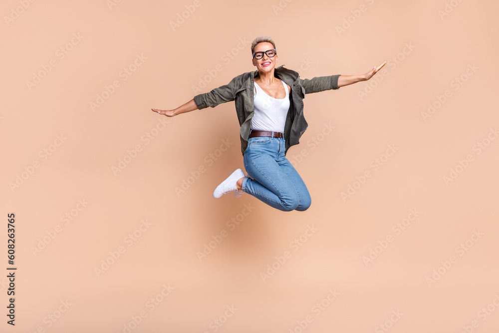 Full length photo of sweet excited lady dressed khaki shirt jumping high arms sides emtpy space isolated beige color background