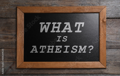 Small chalkboard with phrase What Is Atheism? on wooden background