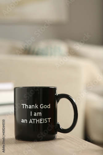 Cup with phrase Thank God I Am Atheist on wooden table