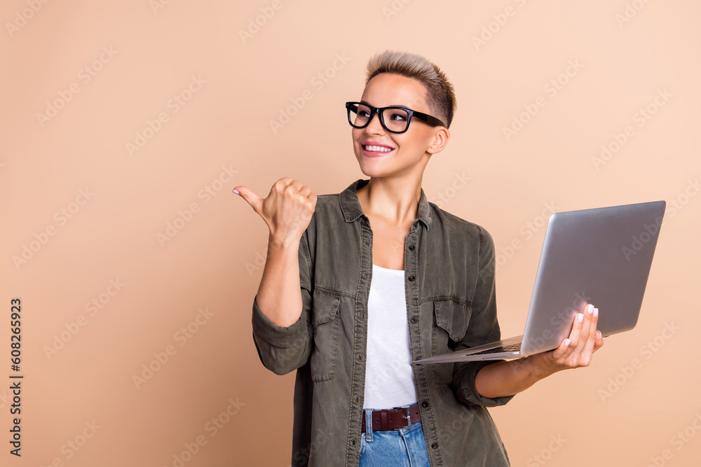 Portrait of charming lady hold netbook look indicate finger empty space isolated on beige color background Portrait of charming lady hold netbook look indicate finger empty space isolated on beige color background