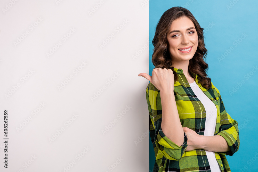 Photo of cute cheerful lady wear checkered jacket pointing thumb back placard empty space isolated blue color background Photo of cute cheerful lady wear checkered jacket pointing thumb back placard empty space isolated blue color background