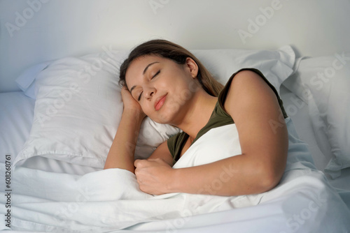 Close-up of Hispanic woman sleeping profoundly in white sheets at night