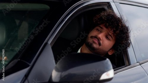 A young man with curly hair sticks his head out of the car window and sighs languidly. An Indian man in a business suit sits in a car and is indignant because of the traffic jam on the road.