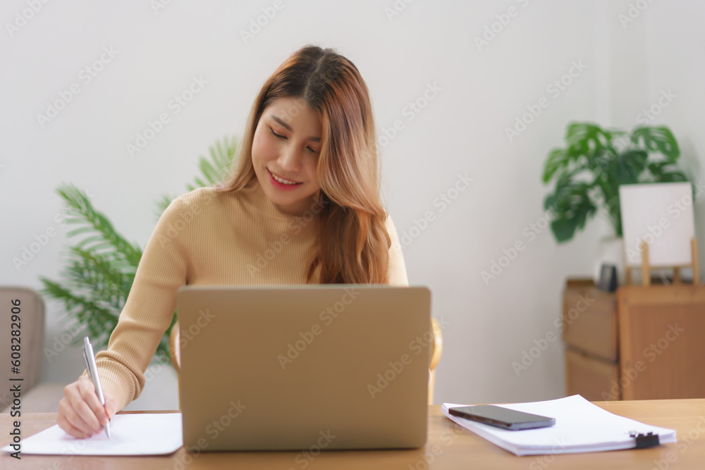 Work from home concept, Businesswoman is reading data on laptop and taking notes on notebook