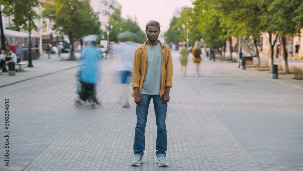 Time lapse portrait of serious Indian man standing in street alone while people moving around. Society and urban lifestyle concept. Time lapse portrait of serious Indian man standing in street alone while people moving around. Society and urban lifestyle concept.