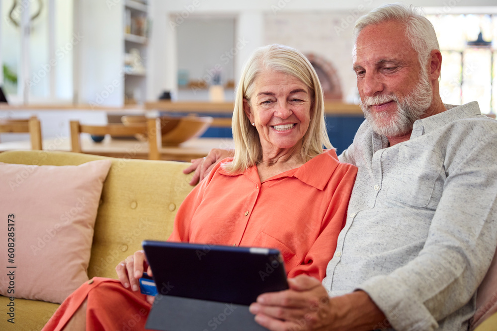 Retired Senior Couple At Home With Digital Tablet Making Purchase Or Booking Using Credit Card Retired Senior Couple At Home With Digital Tablet Making Purchase Or Booking Using Credit Card