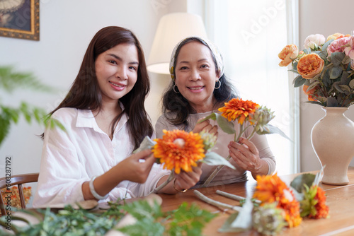 Startup, small business, flower shop. Young and older woman florist putting a flower on a vase
