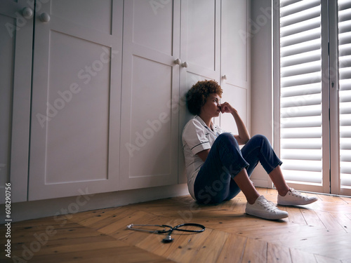 Demotivated Nurse Wearing Uniform Sitting On Floor At Home After Long Shift photo