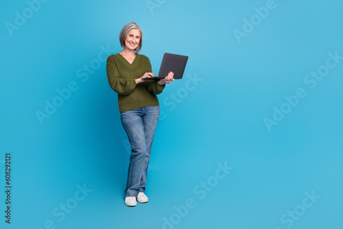 Full body cadre of pensioner old business lady wear khaki sweater hold netbook remote profession worker isolated on blue color background