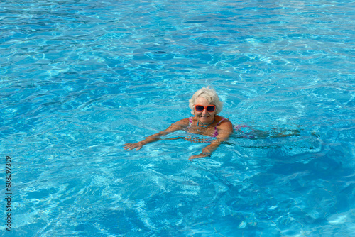 Aged woman is swimming in bright blue water of pool. © vaz1