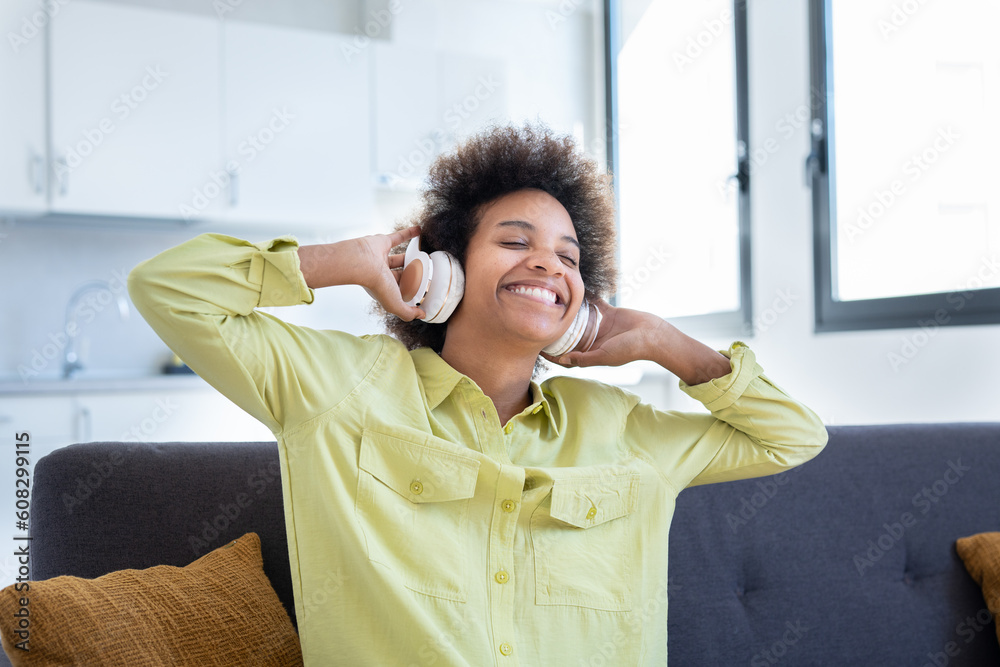 Portrait and close up of one happy and cheerful afro American young woman enjoying and having fun listening music and singing songs at home on the sofa. Carefree lifestyle concept. Portrait and close up of one happy and cheerful afro American young woman enjoying and having fun listening music and singing songs at home on the sofa. Carefree lifestyle concept.