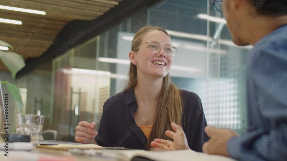 Over the shoulder shot of young cheerful girl smiling and chatting with colleague in office coworking room Over the shoulder shot of young cheerful girl smiling and chatting with colleague in office coworking room