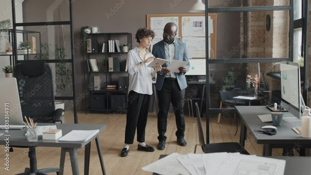 Full shot of female Caucasian office worker approaching colleague showing something in tablet and discussing project Full shot of female Caucasian office worker approaching colleague showing something in tablet and discussing project