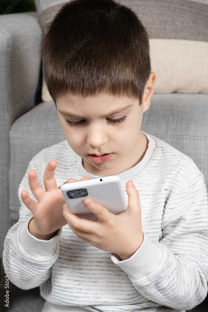 A preschool boy uses a smartphone, plays games on his phone. Screen Time, Parental Controls A preschool boy uses a smartphone, plays games on his phone. Screen Time, Parental Controls