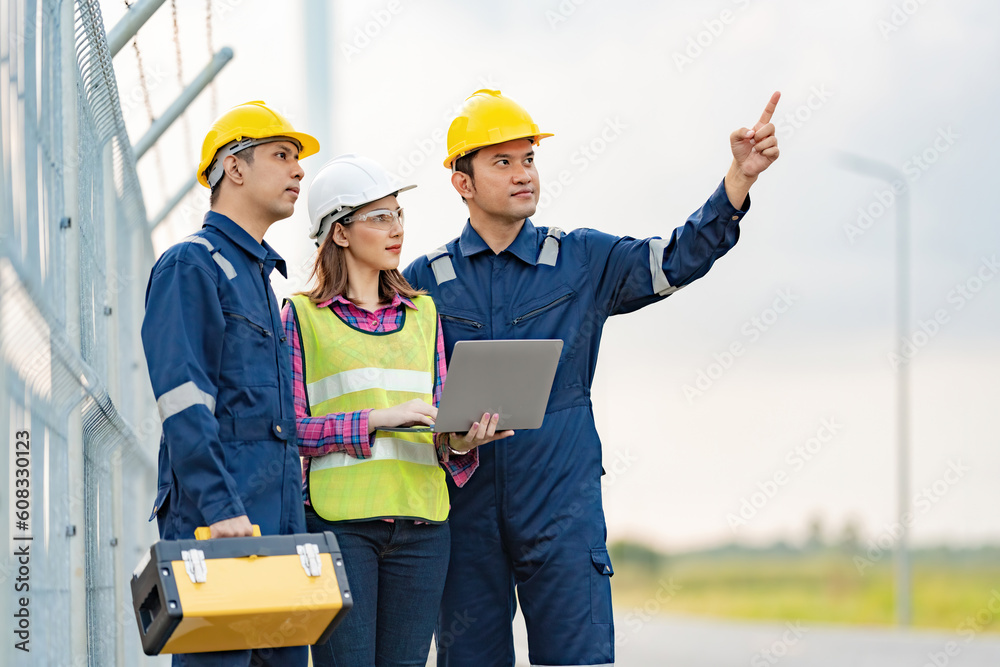 A team of three Asian female mechanics and engineers wearing maintenance suits and vests. point to destination working on tablet near the industrial plant holding a toolbox and wearing a helmet A team of three Asian female mechanics and engineers wearing maintenance suits and vests. point to destination working on tablet near the industrial plant holding a toolbox and wearing a helmet