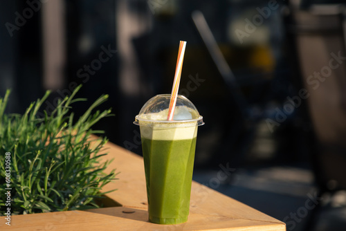 A plastic glass with a green smoothie on the terrace of a cafe. Detox smoothie drink toast on summer vacation, fruit juice weight loss diet.