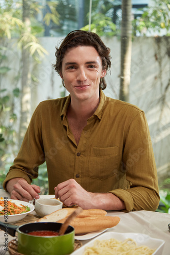 Portrait of happy young man eating tasty homemade dishes