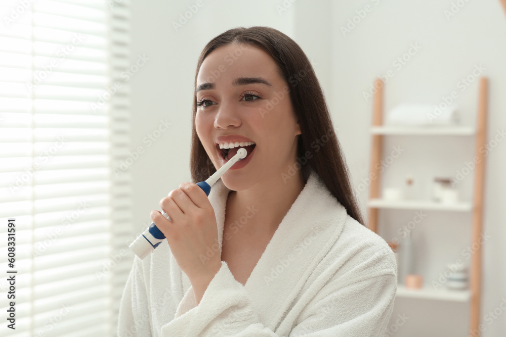 Young woman brushing her teeth with electric toothbrush in bathroom Young woman brushing her teeth with electric toothbrush in bathroom