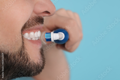 Man brushing his teeth with electric toothbrush on light blue background, closeup. Space for text