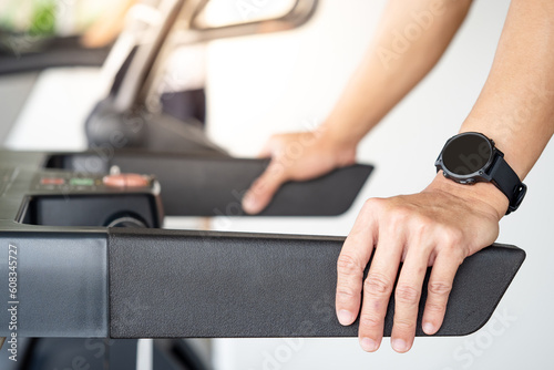 Runner man wearing smartwatch while using treadmill running in fitness gym. Wearable device for sport activity. Smart watch technology for health tracking. Healthy lifestyle concept. © Summer Paradive
