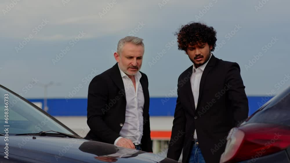 Two businessmen are looking at the car damage at the parking lot. Two men in suits are debating at the parking Two businessmen are looking at the car damage at the parking lot. Two men in suits are debating at the parking