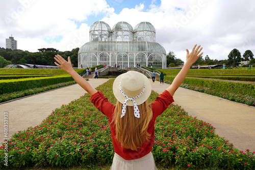 Tourism in Curitiba, Brazil. Back view of stylish traveler woman with raising arms in  botanical garden of Curitiba, Parana, Brazil. photo