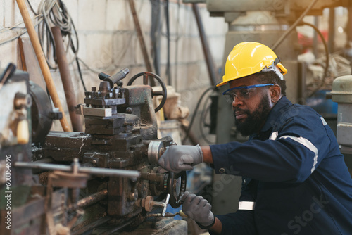 Male factory worker working at work maintenance machine in industrial factory while wearing safety uniform, glasses and hard hat. Black male technician and heavy steel lathe machine in workshop