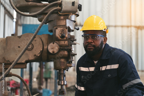 Male factory worker working at work maintenance machine in industrial factory while wearing safety uniform, glasses and hard hat. Black male technician and heavy steel lathe machine in workshop