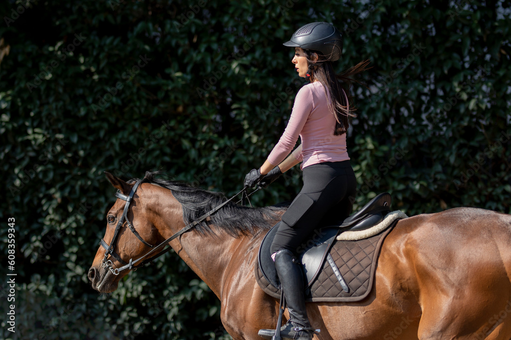 Side shot of a woman riding a horse with bushes in the background