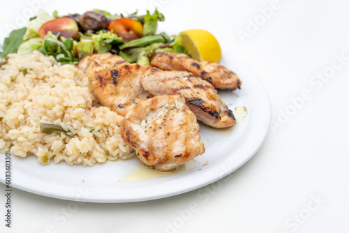 Roasted chicken fillet with rice, mixed salad and lemon, Mediterranean meal served on a plate, white table, copy space, selected focus